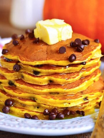 stack of pumpkin pancakes with chocolate chips on a plate with a pat of butter on top and a drizzle of syrup