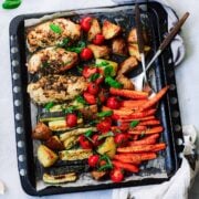 top view of a sheet pan with chicken breasts, carrots, zucchini, and potatoes