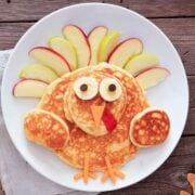 a thanksgiving turkey pancake on a plate made with pancakes and fruit to resemble a turkey
