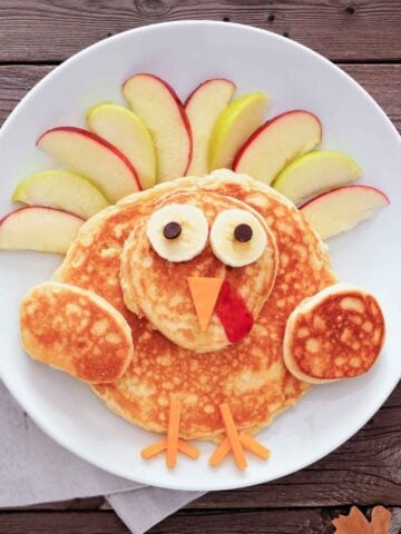 a thanksgiving turkey pancake on a plate made with pancakes and fruit to resemble a turkey