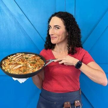 Laura fuentes holding a skillet of food standing in front of a blue door