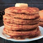 stack of pumpkin oatmeal pancakes on a plate topped with some butter and drizzled with syrup