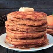 stack of pumpkin oatmeal pancakes on a plate topped with some butter and drizzled with syrup