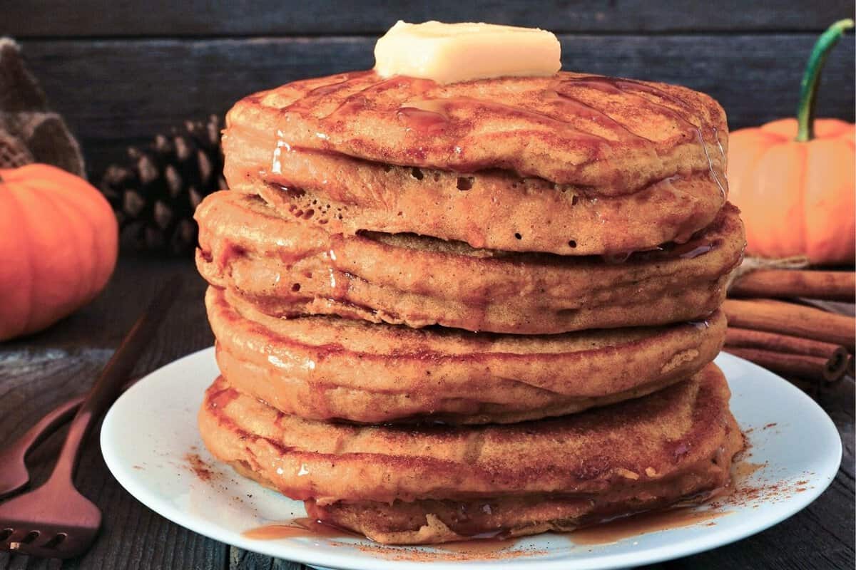 stack of pumpkin oatmeal pancakes on a plate topped with some butter and drizzled with syrup