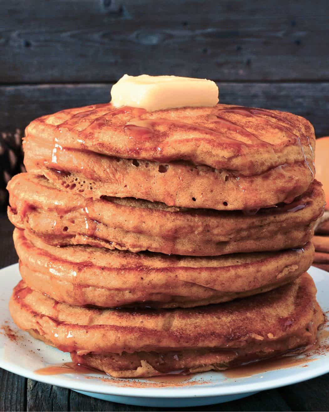 stack of pumpkin oatmeal pancakes on a plate topped with some butter and drizzled with syrup