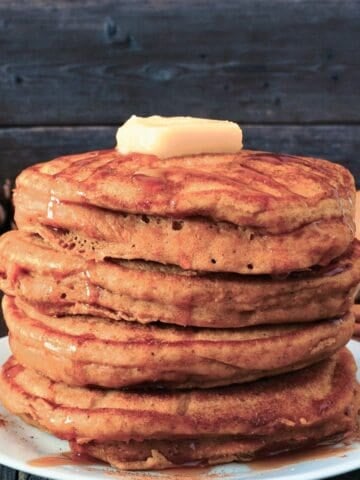 stack of pumpkin oatmeal pancakes on a plate topped with some butter and drizzled with syrup