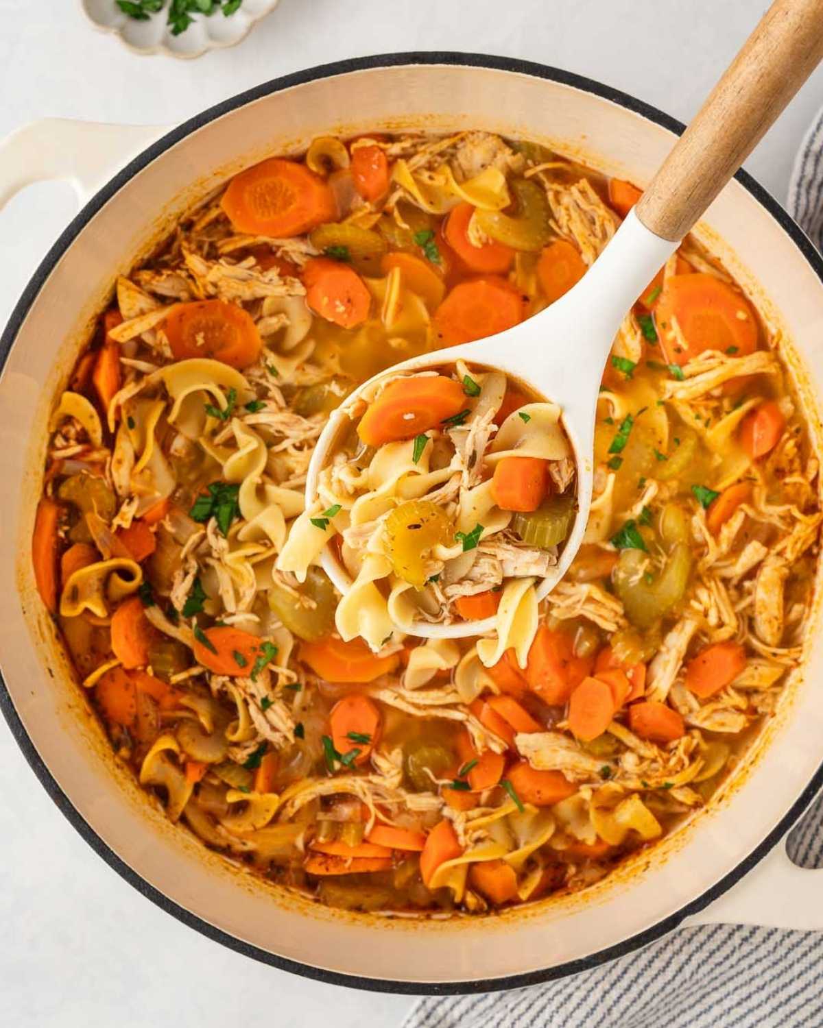 overhead view of ladling out spicy chicken noodle soup from a dutch oven pot