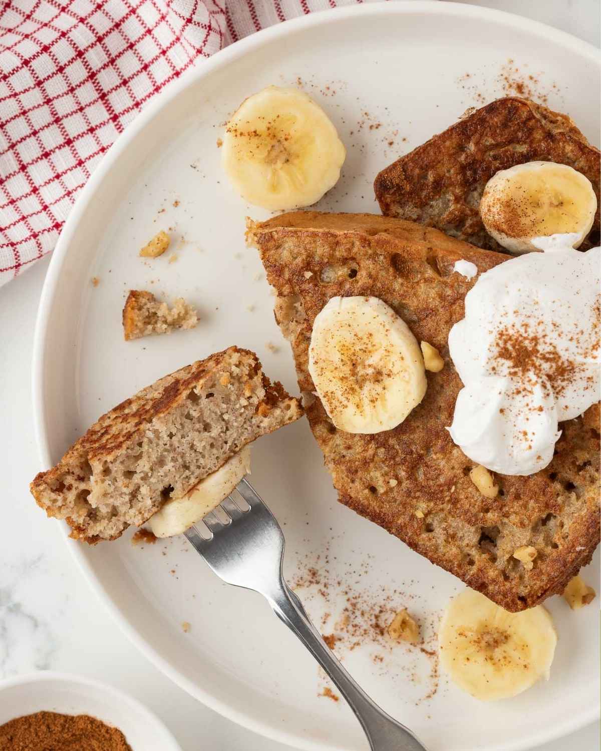top view of banana bread french toast sliced on a fork topped with banana slices and whipped cream