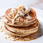 a stack of granola pancakes topped with slivered almonds and whipped cream
