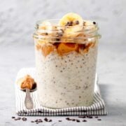 a jar of overnight oats topped with banana slices and peanut butter next to a spoon with peanut butter