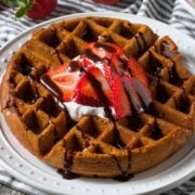 overhead view of chocolate waffles topped with a little cream, sliced strawberries, and a drizzle of chocolate syrup