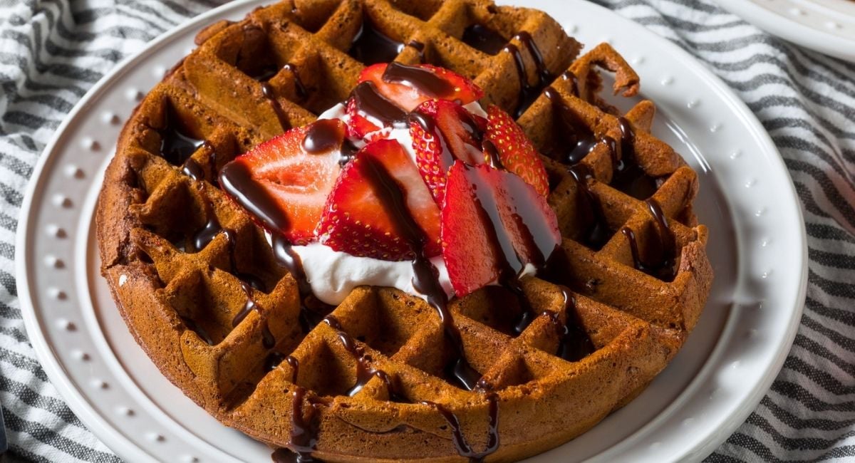 overhead view of chocolate waffles topped with a little cream, sliced strawberries, and a drizzle of chocolate syrup