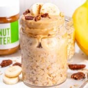 a jar or peanut butter banana overnight oats topped with sliced bananas and chopped pecans
