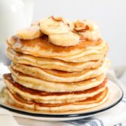 stack of banana pancakes made with pancake mix on a plate topped with sliced bananas, chopped nuts, and pancake syrup