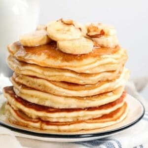 stack of banana pancakes made with pancake mix on a plate topped with sliced bananas, chopped nuts, and pancake syrup