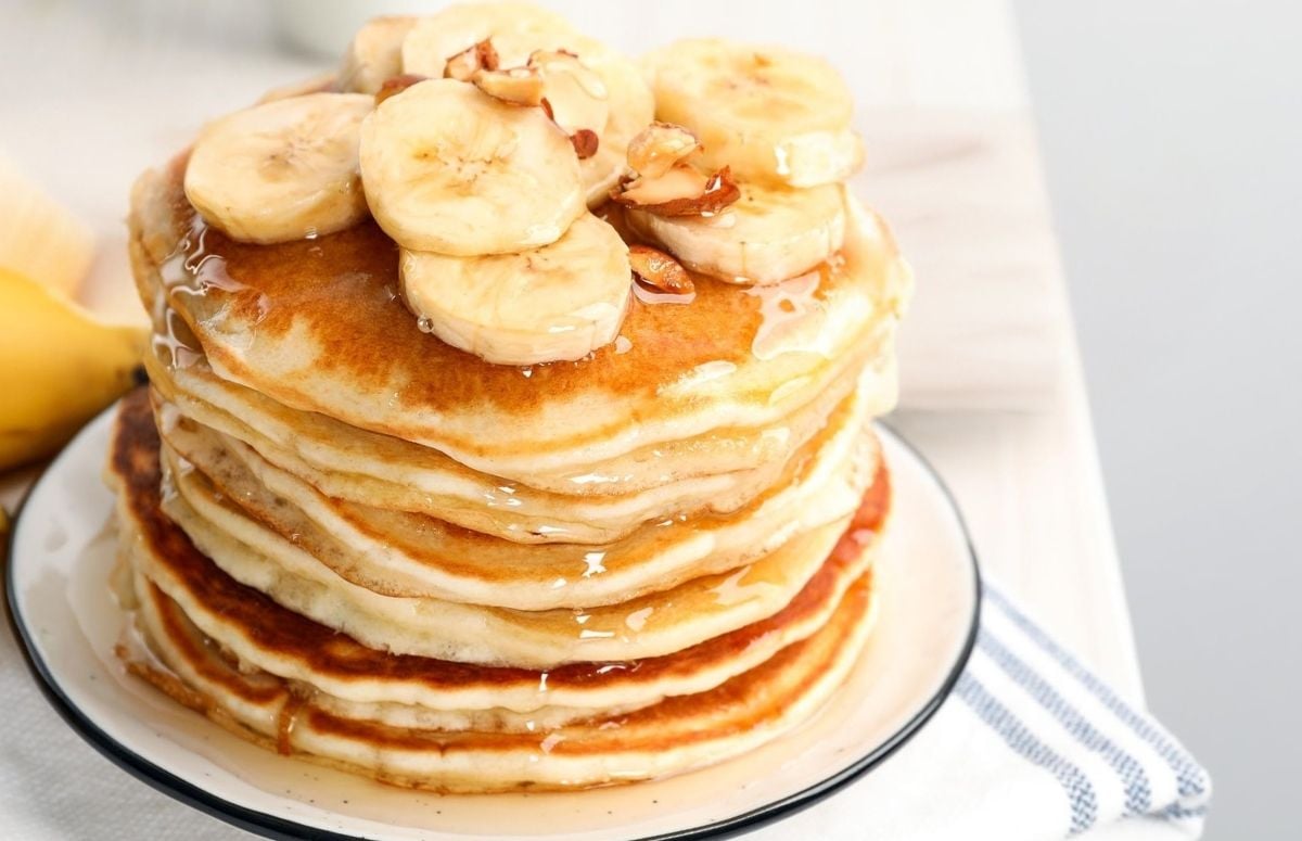stack of banana pancakes made with pancake mix on a plate topped with sliced bananas, chopped nuts, and pancake syrup