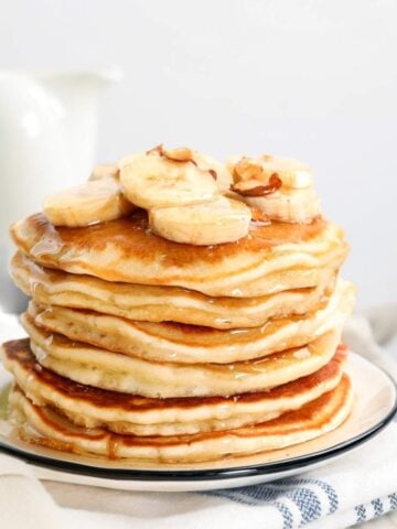 stack of banana pancakes made with pancake mix on a plate topped with sliced bananas, chopped nuts, and pancake syrup