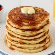 large stack of buttermilk pancakes topped with syrup and butter