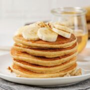 Stack of gluten-free banana pancakes on a plate topped with sliced bananas and a light drizzle of syrup