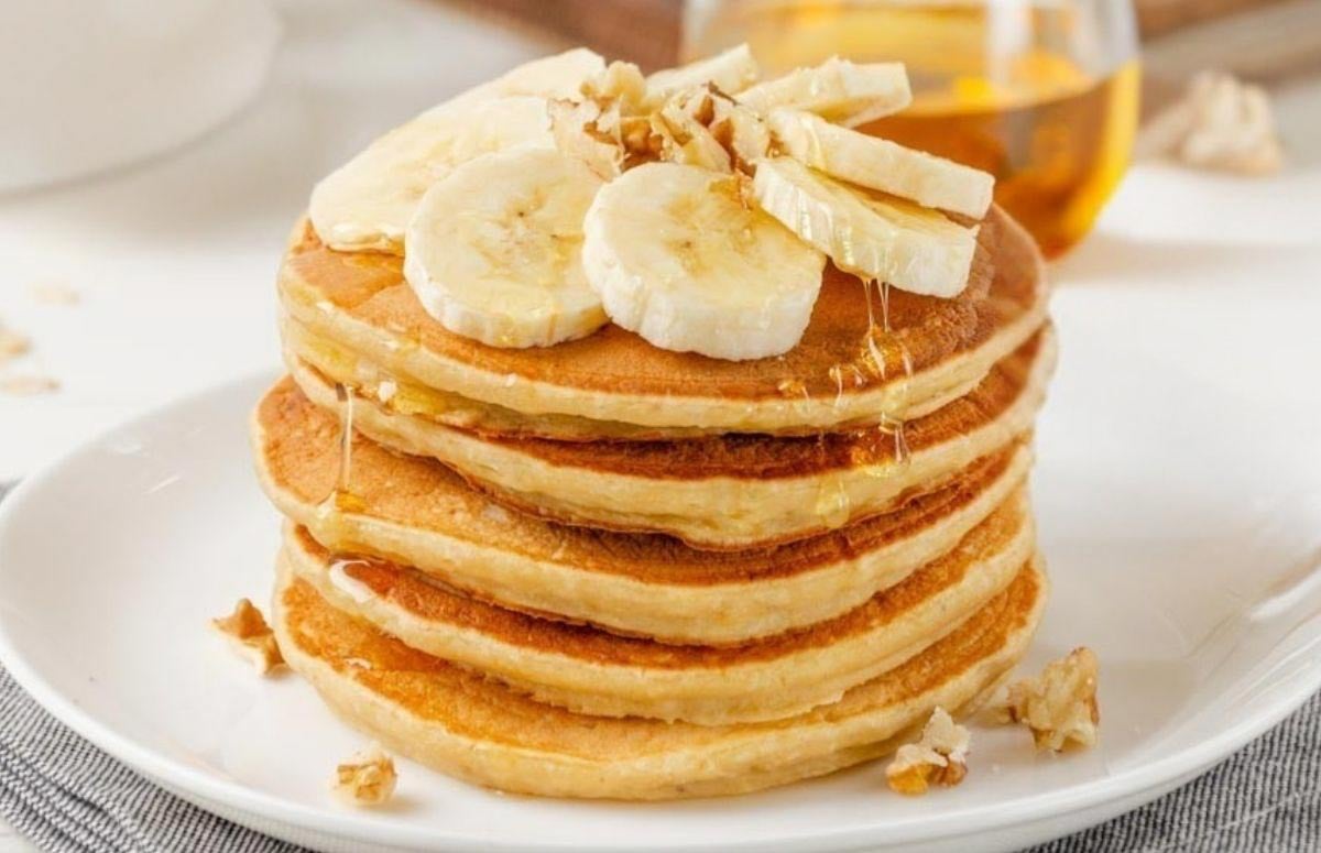 Stack of gluten-free banana pancakes on a plate topped with sliced bananas and a light drizzle of syrup