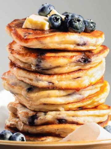 large stack of lemon blueberry ricotta pancakes topped with butter and blueberries