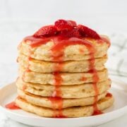 stack of fluffy pancakes topped with strawberries and strawberry syrup