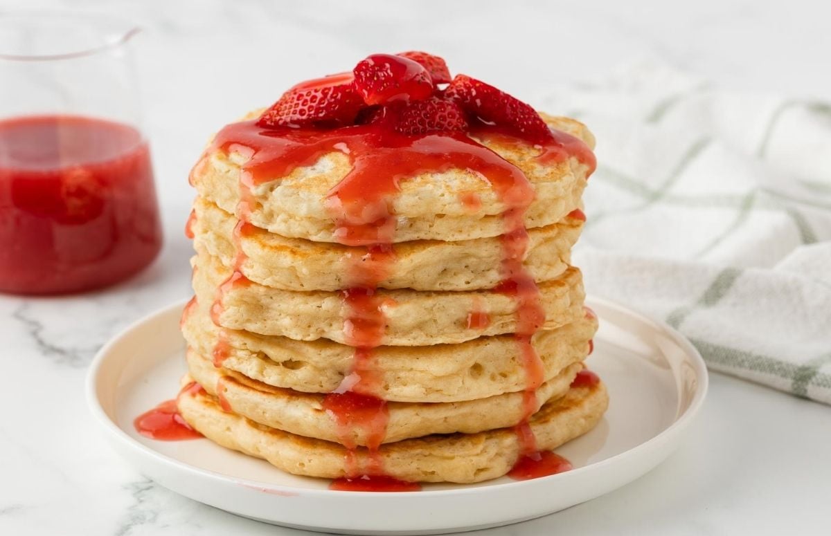 stack of fluffy pancakes topped with strawberries and strawberry syrup