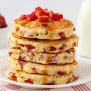 Front view of a fluffy stack of strawberry pancakes topped with more diced strawberries and a light drizzle of pancake syrup