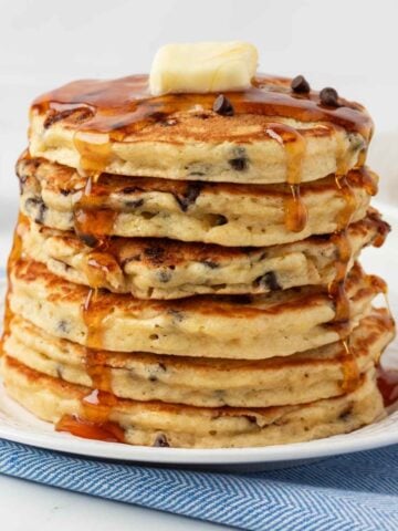 Stack of cookie pancakes with chocolate chips on a plate topped with butter and pancake syrup