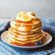 stack of banana ricotta pancakes on a plate topped with sliced bananas and pancake syrup