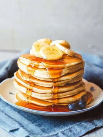 stack of banana ricotta pancakes on a plate topped with sliced bananas and pancake syrup