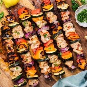 overhead view of grilled chicken kabobs on a cutting board. Each skewer has chicken and veggies (bell peppers, onions, and zucchini) threaded through.