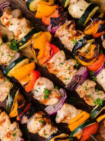 overhead view of grilled chicken kabobs on a cutting board. Each skewer has chicken and veggies (bell peppers, onions, and zucchini) threaded through.