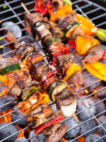 meat and vegetable kabobs threaded through skewers on a grill