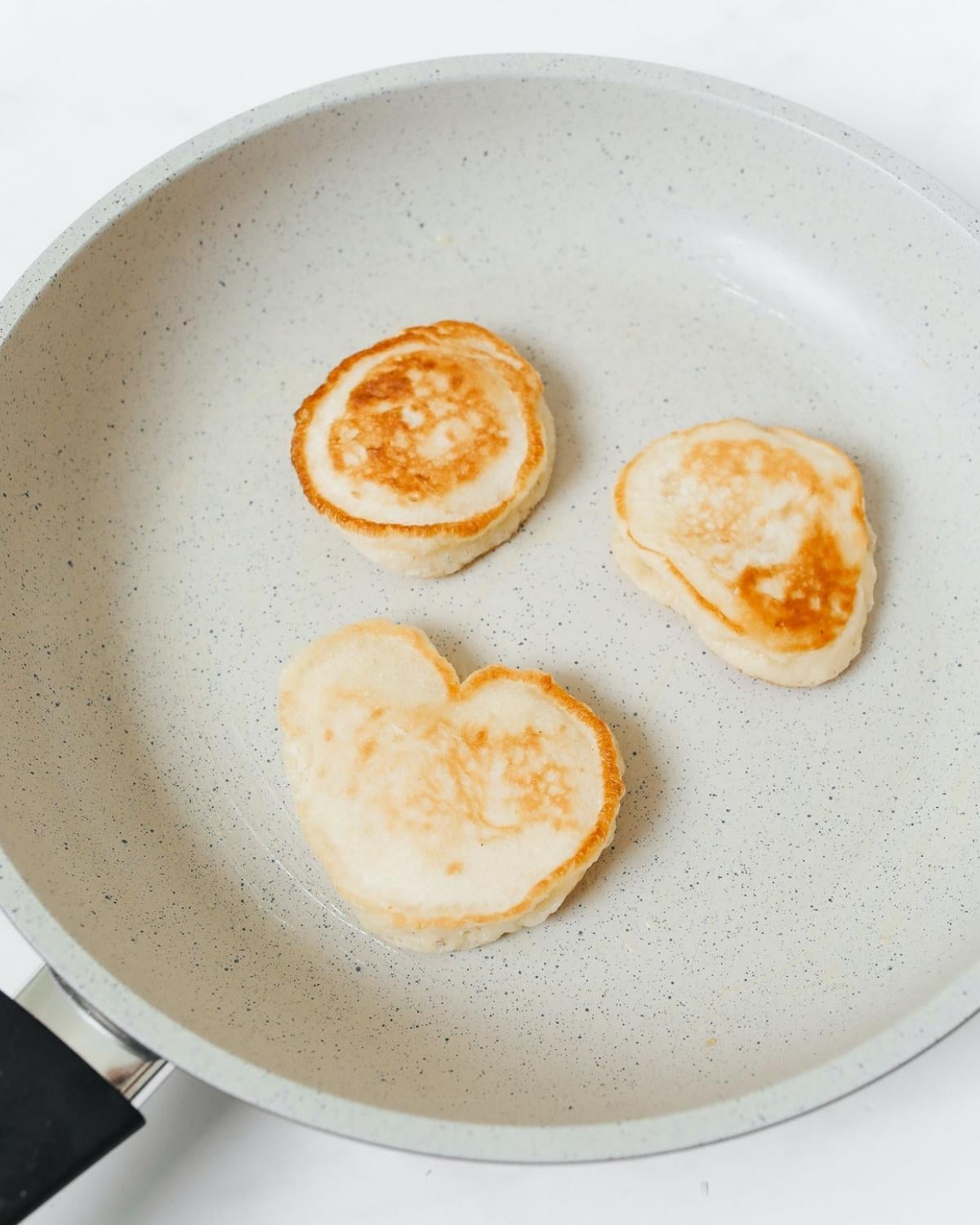 3 small pancakes cooking on a nonstick pan.