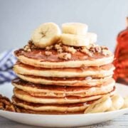stack of vegan pancakes on a plate topped with sliced bananas and chopped nuts.