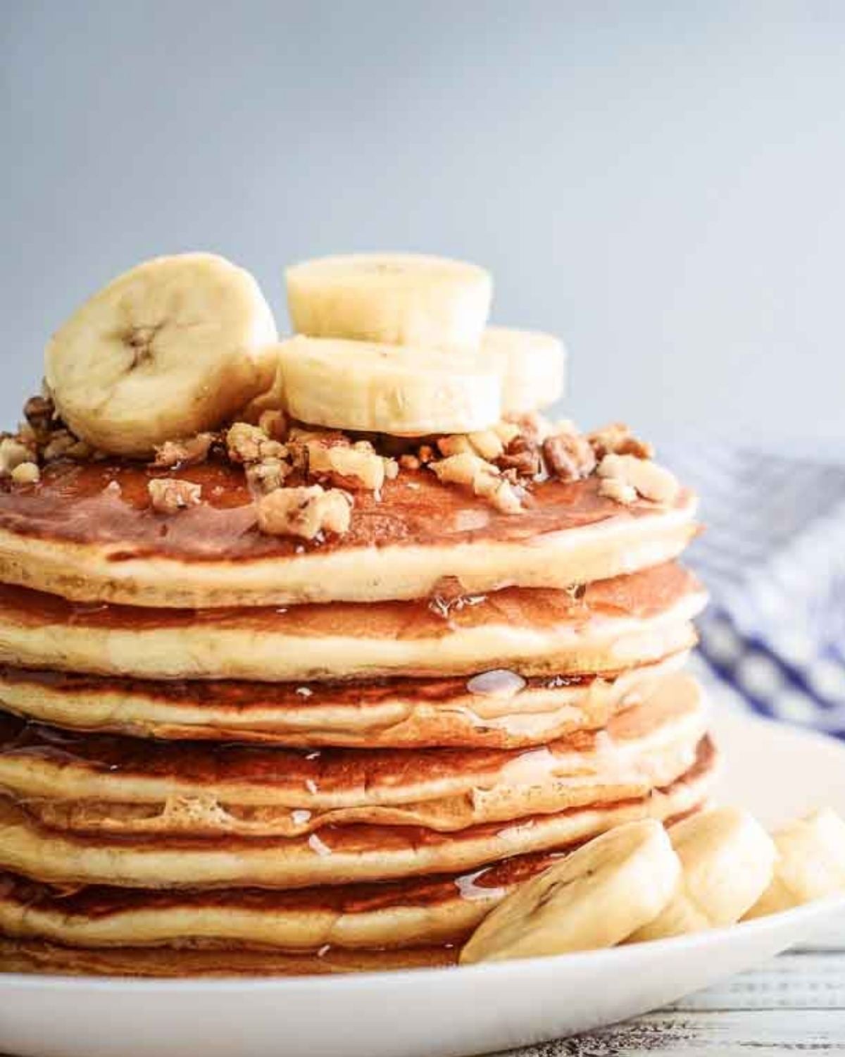 stack of vegan pancakes on a plate topped with sliced bananas and chopped nuts.