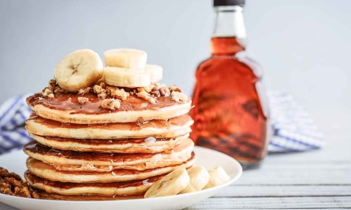 stack of vegan pancakes on a plate topped with sliced bananas and chopped nuts.