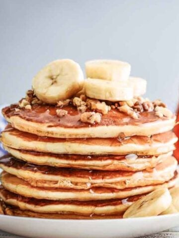 stack of vegan pancakes on a plate topped with sliced bananas and chopped nuts.