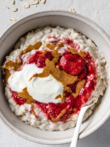 a bowl of oatmeal topped with Greek yogurt, peanut butter, and strawberries