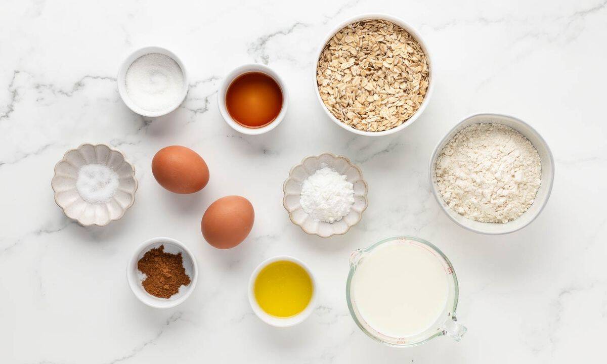 Ingredients for oatmeal pancakes, including oats, flour, eggs, milk, sugar, baking powder, vanilla, melted butter, cinnamon, and salt.