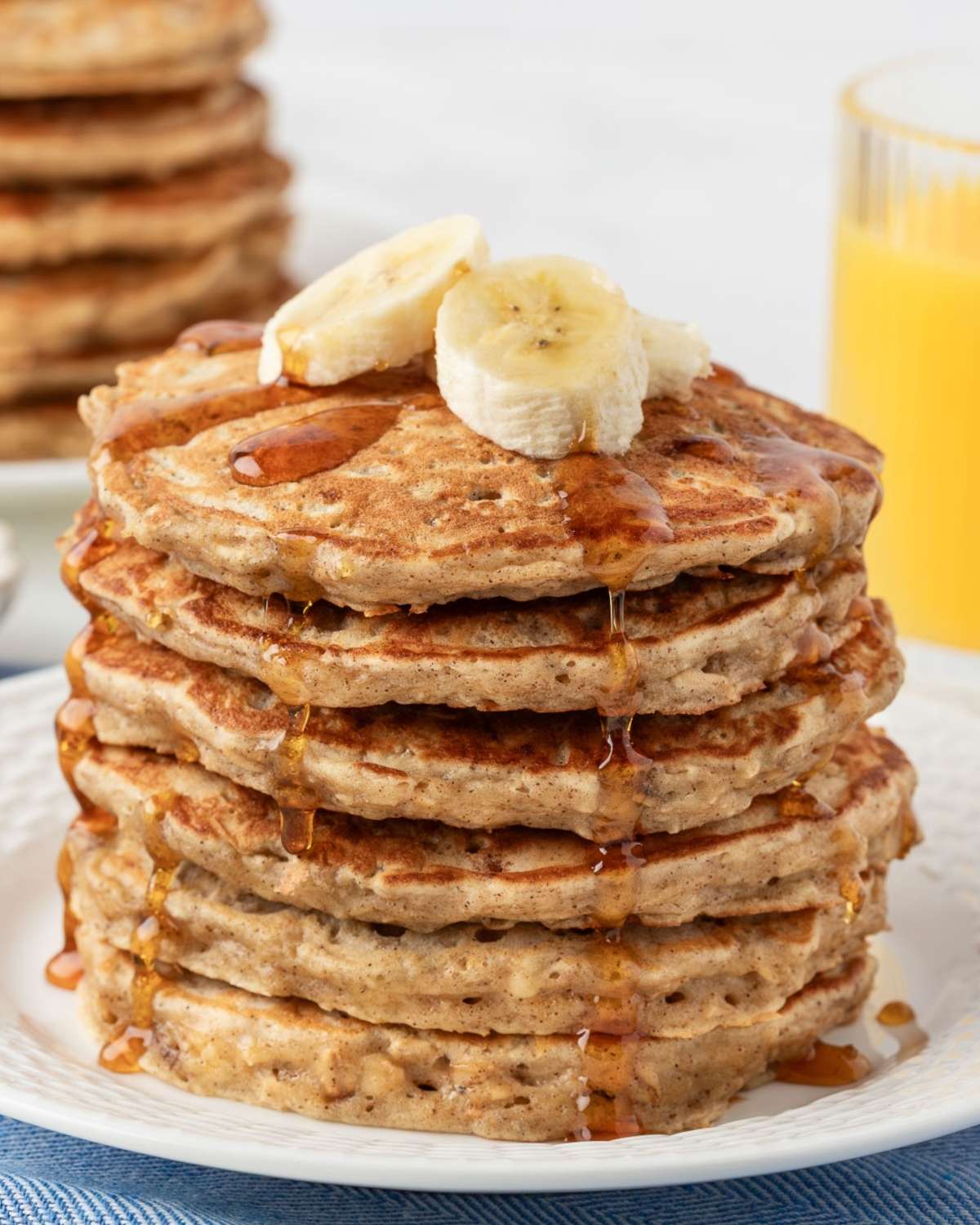 stack of banana oatmeal pancakes on a plate topped with sliced bananas and a drizzle of pancake syrup