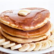 stack of banana ricotta pancakes on a plate with sliced bananas and pancake syrup
