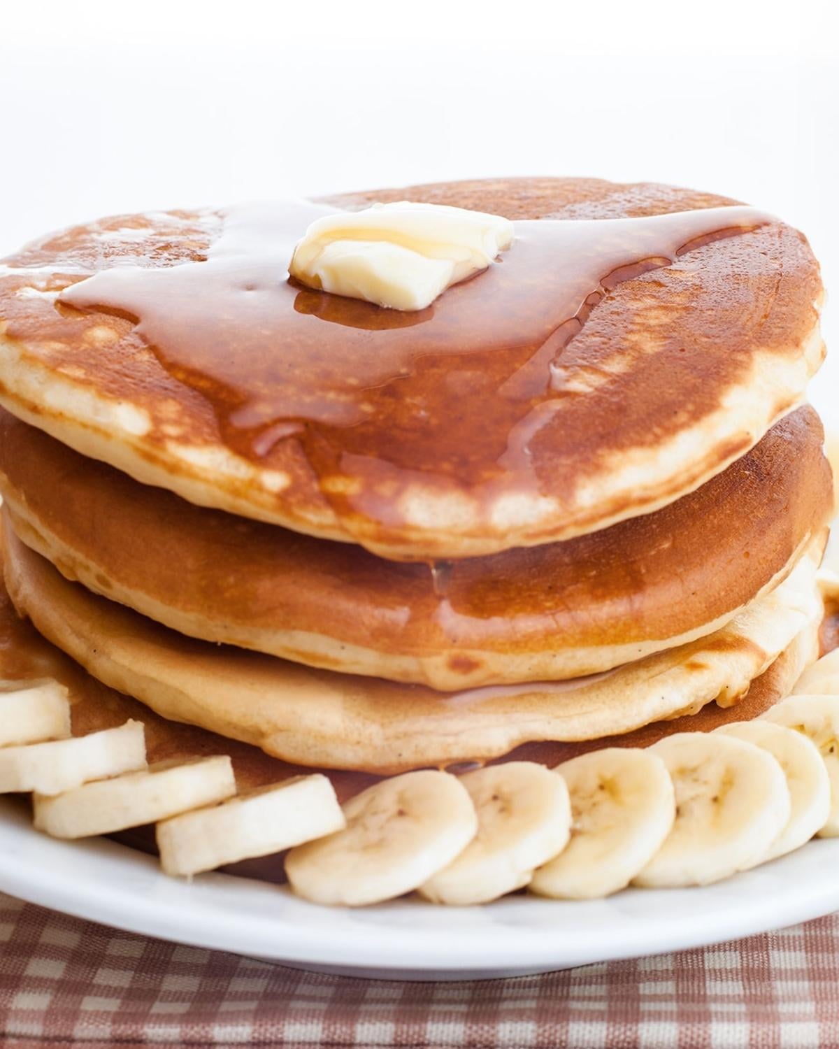 stack of banana ricotta pancakes on a plate with sliced bananas and pancake syrup