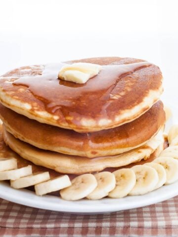 stack of banana ricotta pancakes on a plate with sliced bananas and pancake syrup