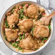 overhead view of a skillet with chicken thighs and rice with peas.