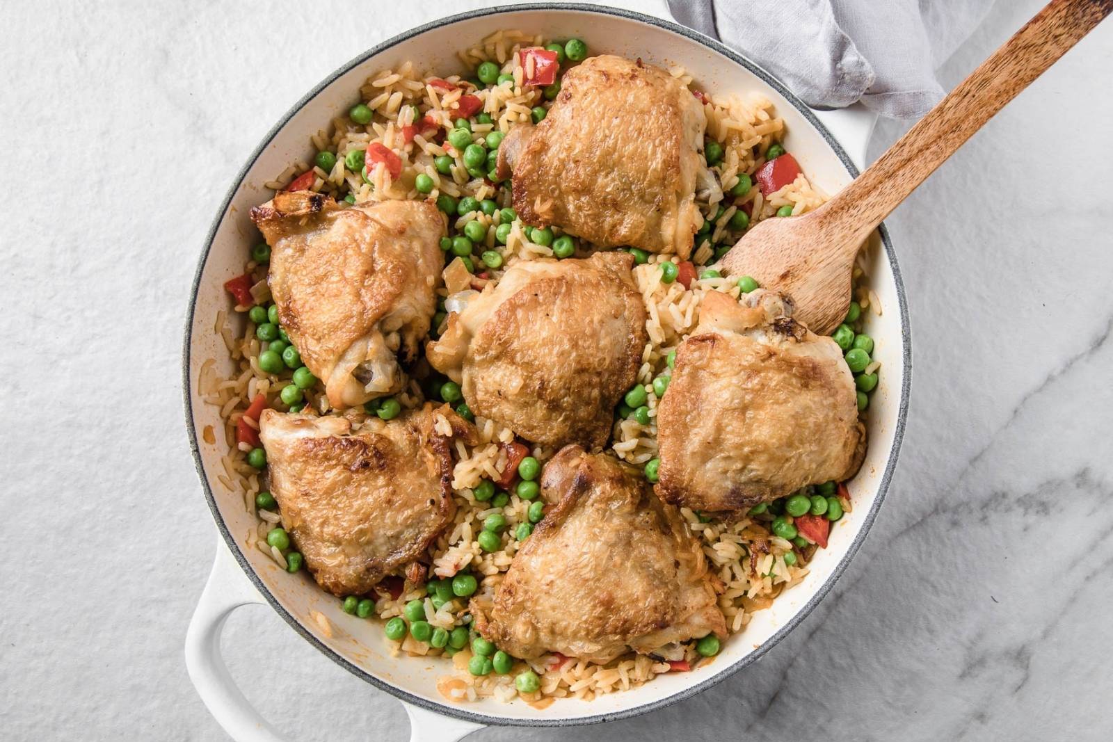overhead view of a skillet with chicken thighs and rice with peas.
