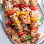 grilled kabobs made with pork, yellow and red bell pepper and served on a white dish