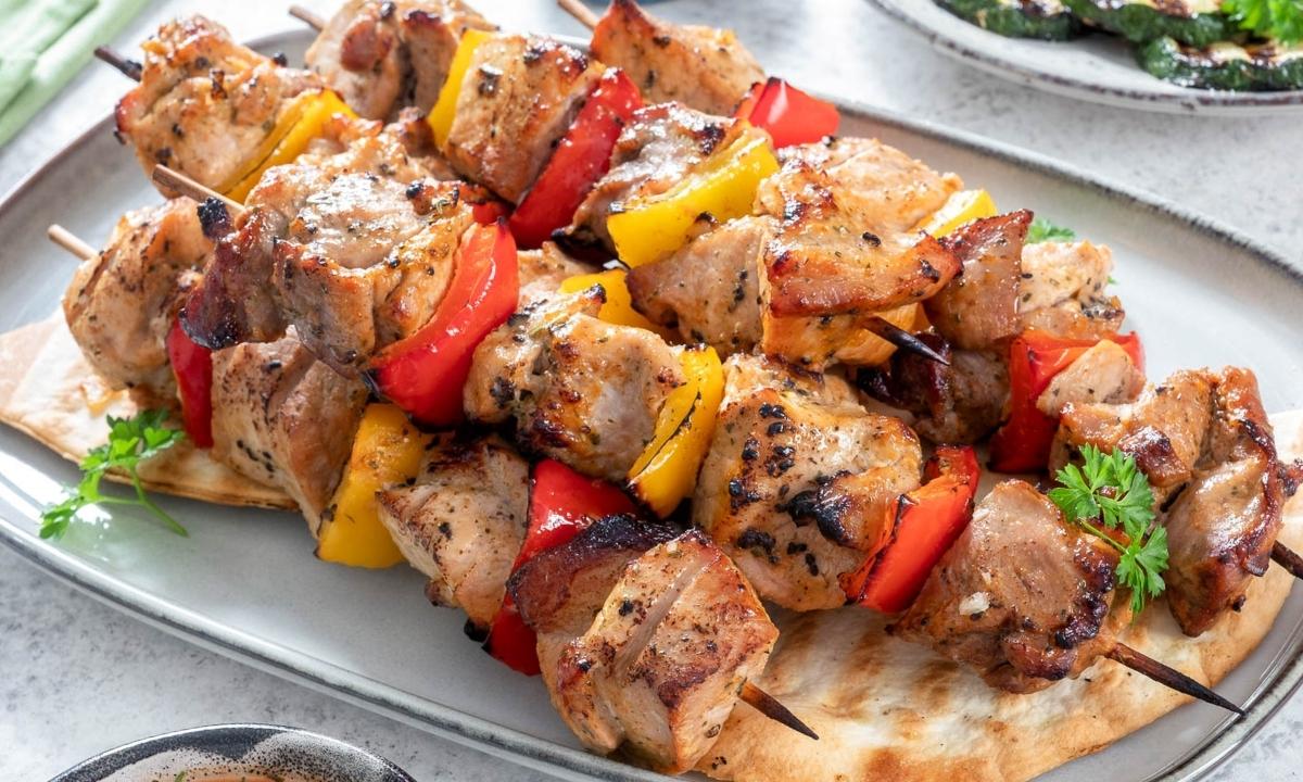 a white dish with five grilled pork bell pepper kabobs