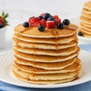 fluffy stack of pancakes made with rice flour on a plate. topped with diced strawberries and blueberries and drizzled with pancake syrup